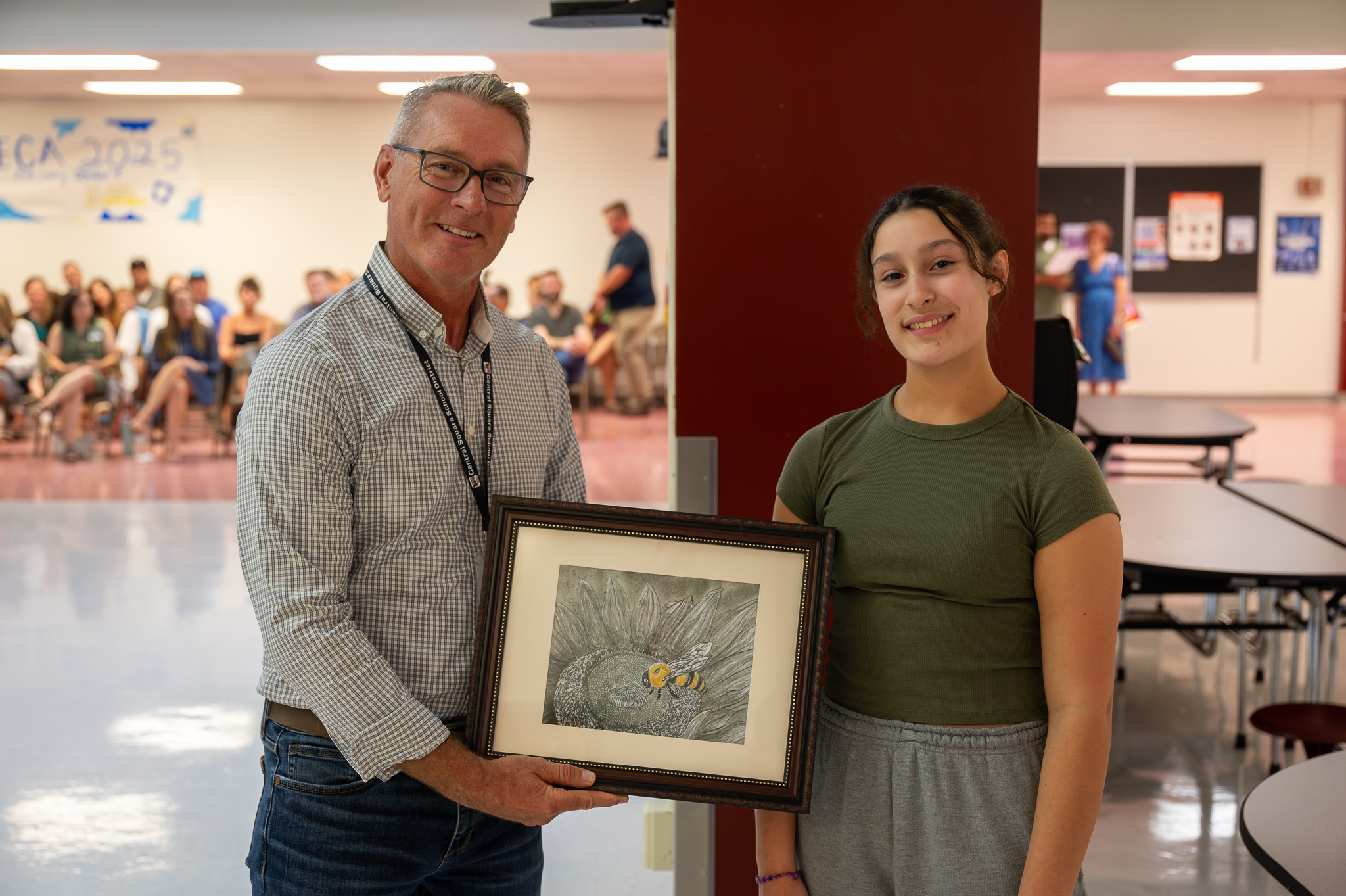 A board of education member standing proudly with a student, who gifted them artwork.